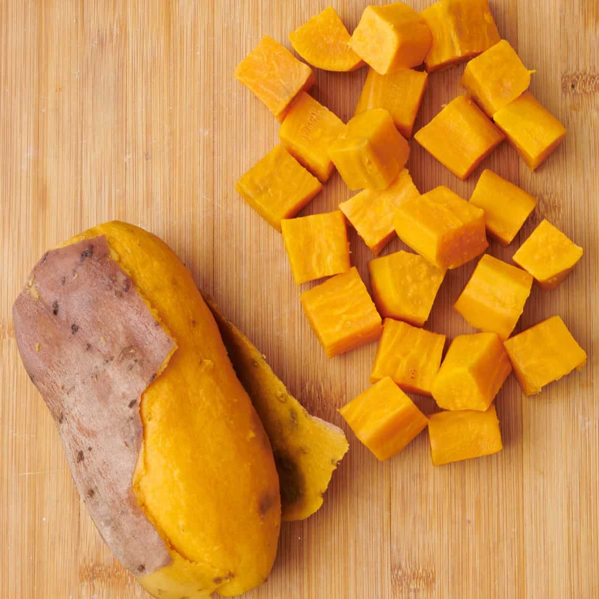Boiled sweet potatoes on a cutting board 2 ways: whole and cubed.