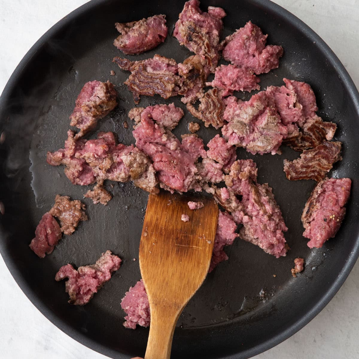 Beef being broken up with a spatula with the bottom browned.