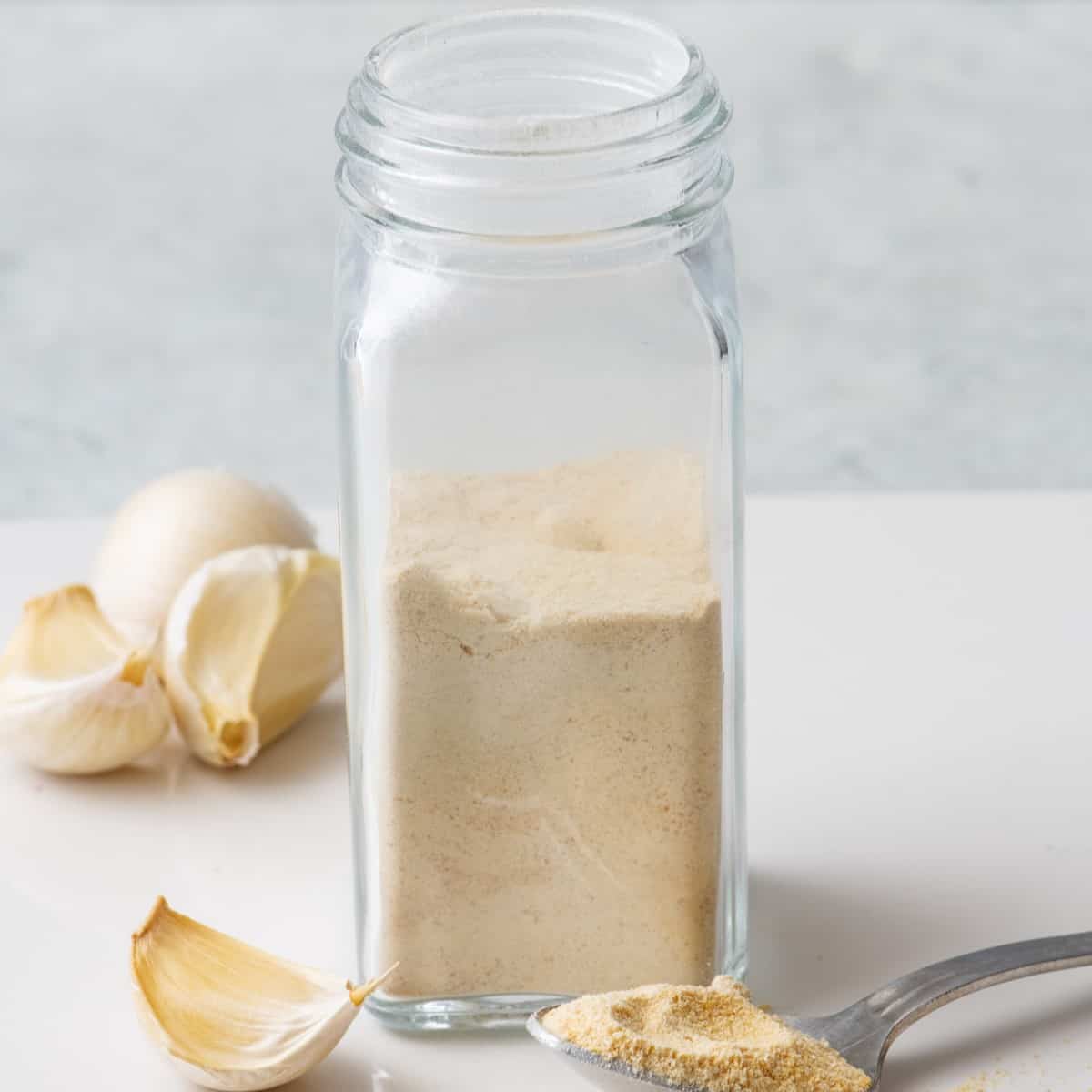 Garlic powder made from garlic cloves in a spice jar with more cloves nearby.