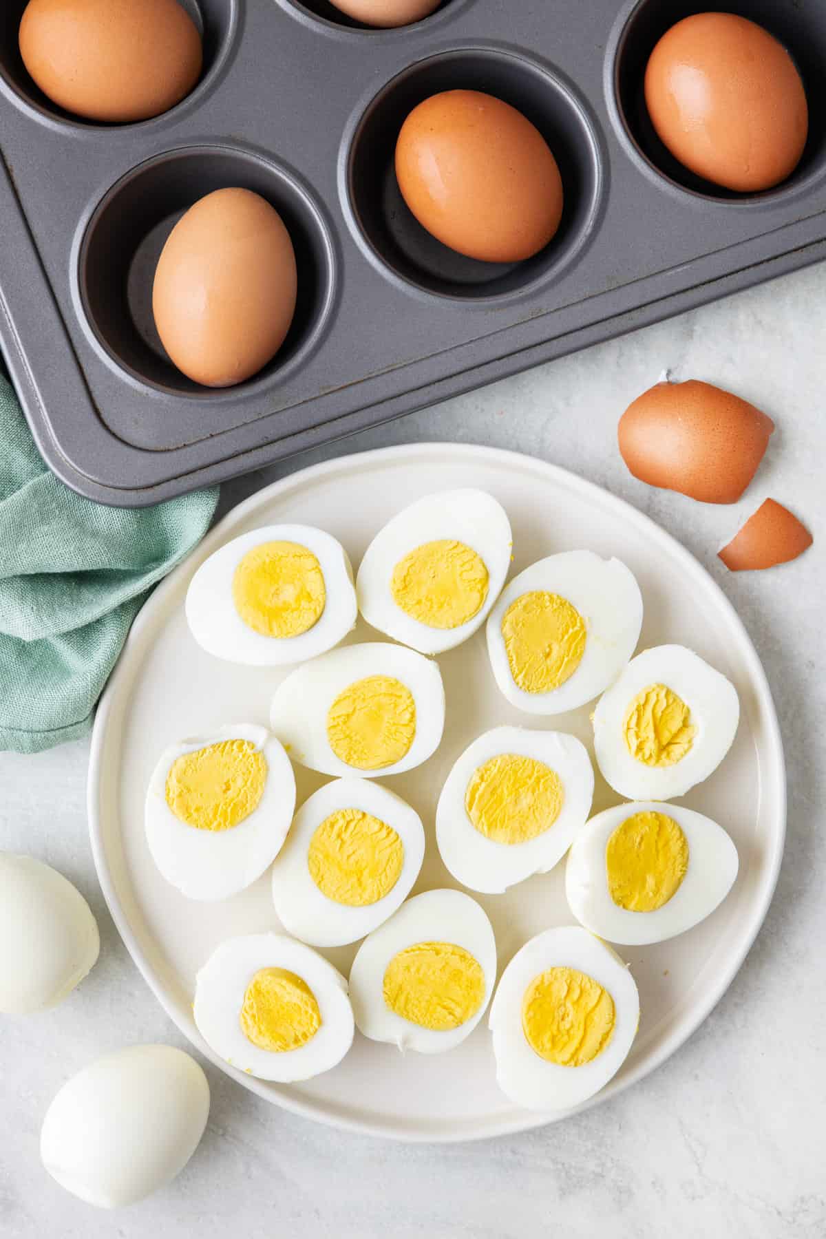 Hard boiled eggs on a plate split in half, with muffin pan of whole baked eggs in shell nearby.