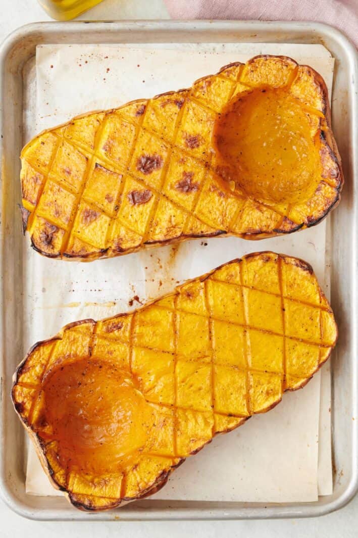 Roasted butternut squash halves scored with diagonal cuts on a sheet pan.