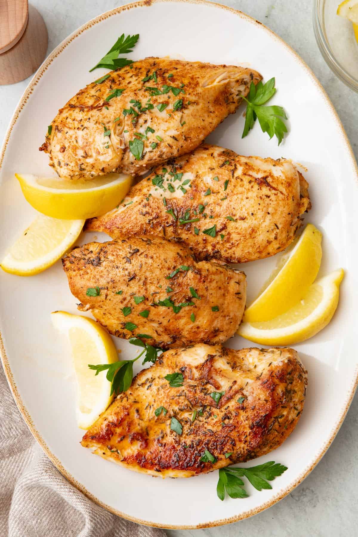 Pan seared chicken breast on a large oval platter, garnished with fresh parsley and lemon wedges.