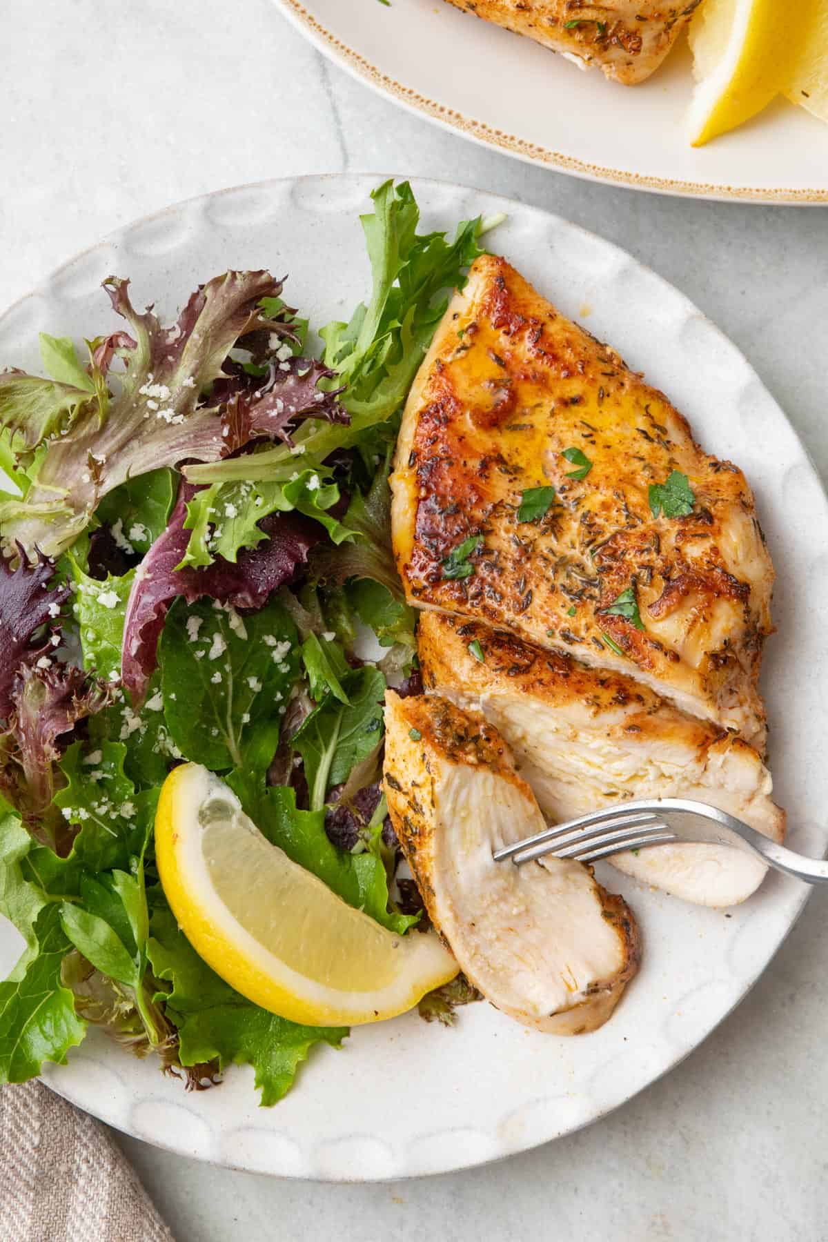 Juicy pan seared chicken on a plate cut into slices about halfway up next to a spring mix salad.