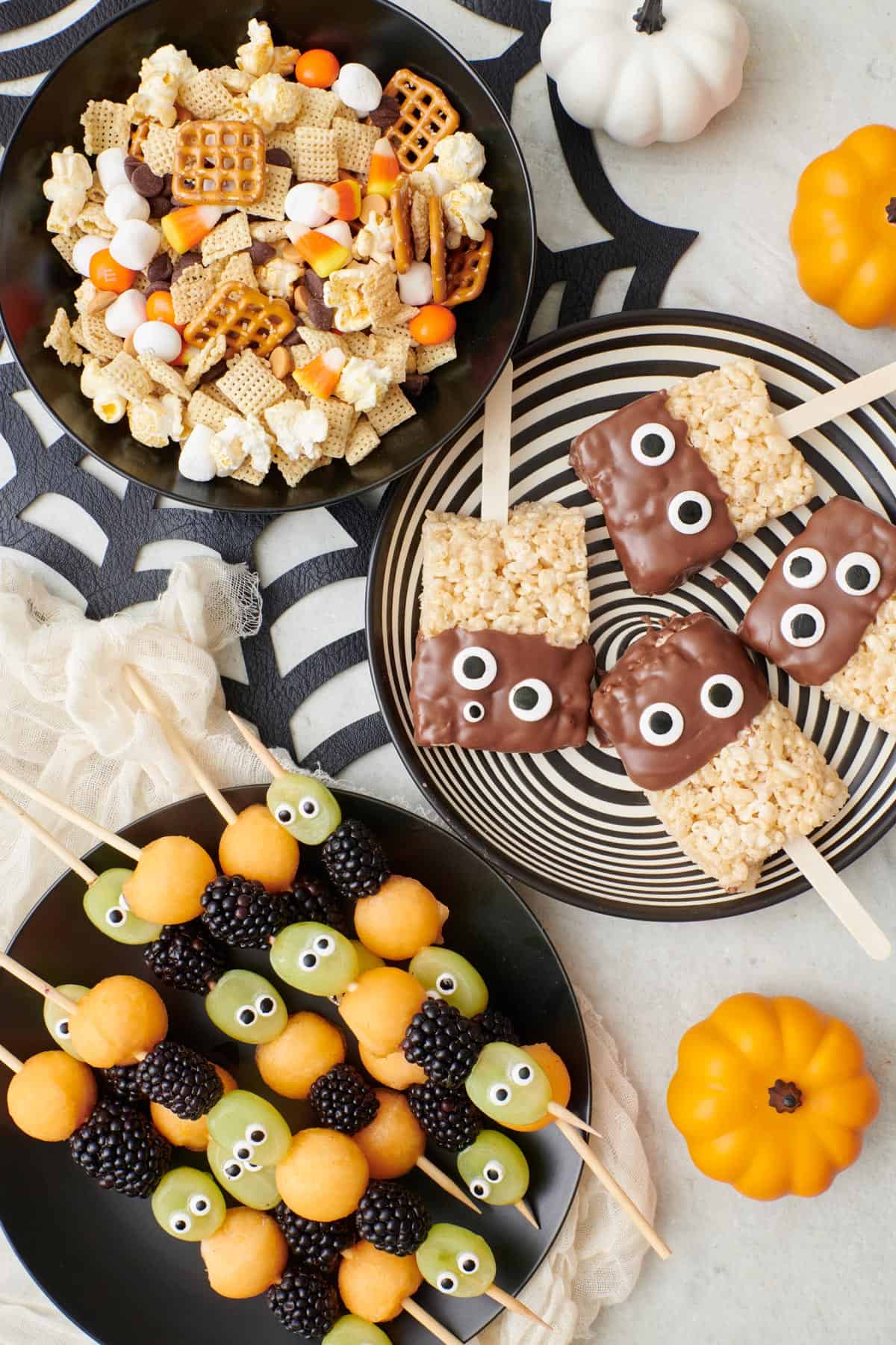 Halloween treats in individual dishes: monster munch, monster rice krispies, and halloween fruit kabobs.