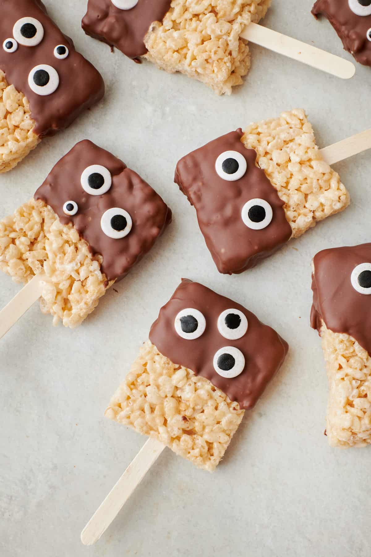 Monster rice krispie treats dipped in chocolate with googly eyes and on a stick.