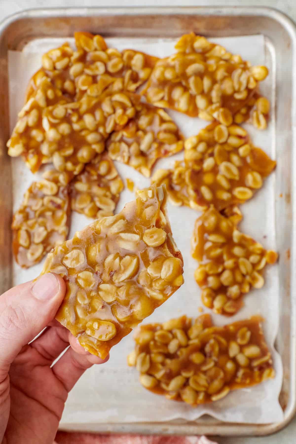 Hand holding a piece of peanut brittle over a pan of more.