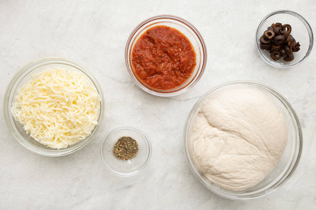 Ingredients for recipe: shredded mozzarella, pizza sauce, oregano, black olives and pizza dough.