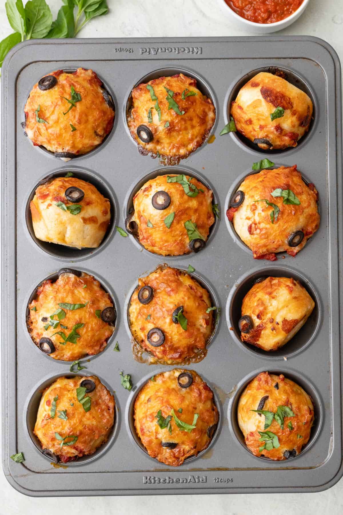 Pizza muffins after baking in a muffin pan to show browned cheese.