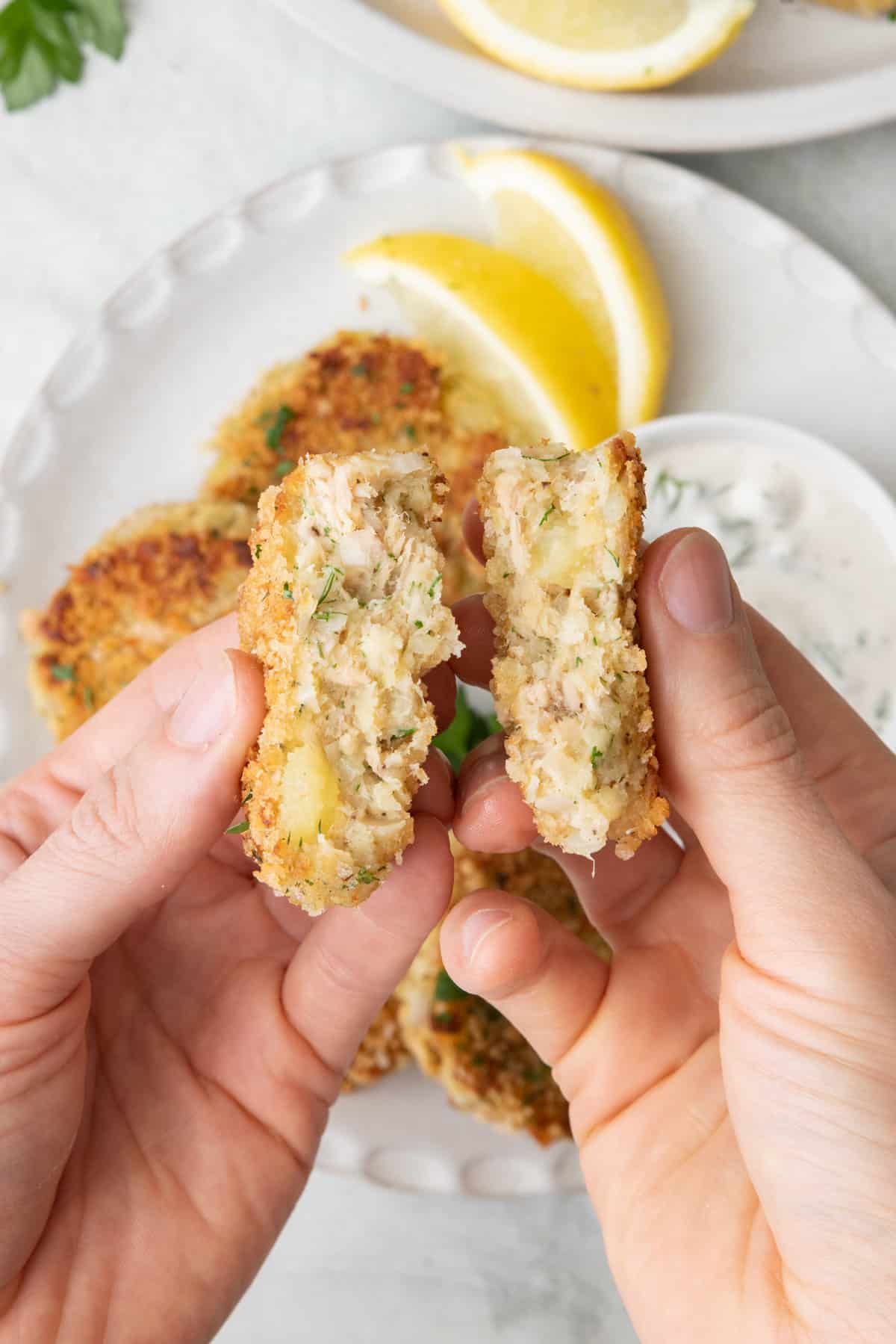 Hand holding two halves of a potato tuna cake to show inside texture.