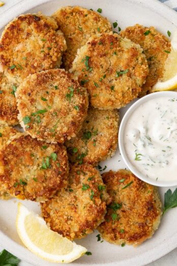 Potato tuna cakes on a plate with a small dish of Tzatziki sauce.