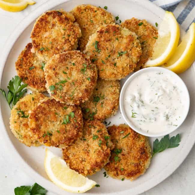 Potato tuna cakes on a plate with a small dish of Tzatziki sauce.