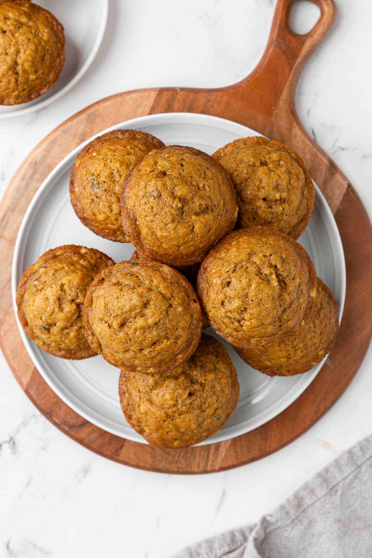 Pumpkin banana muffins stacked on a round plate on a decorative board.