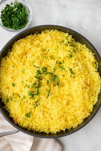 Saffron rice in pot after being fluffed and garnished with fresh parsley.