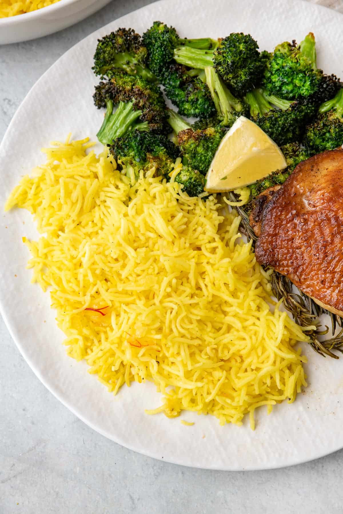 Saffron rice on a plate next to broccoli and a chicken thigh.