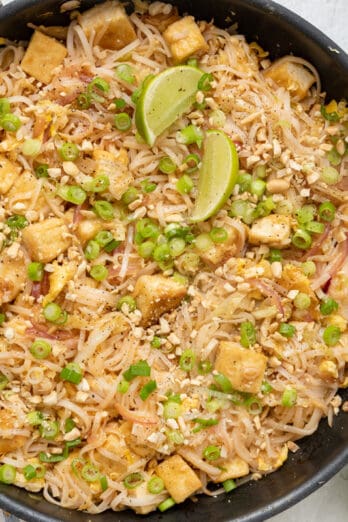 Vegetarian pad thai with tofu garnished with green onions and lemon wedges.