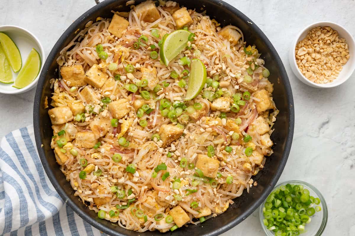 Vegetarian pad thai with tofu garnished with green onions and lemon wedges.