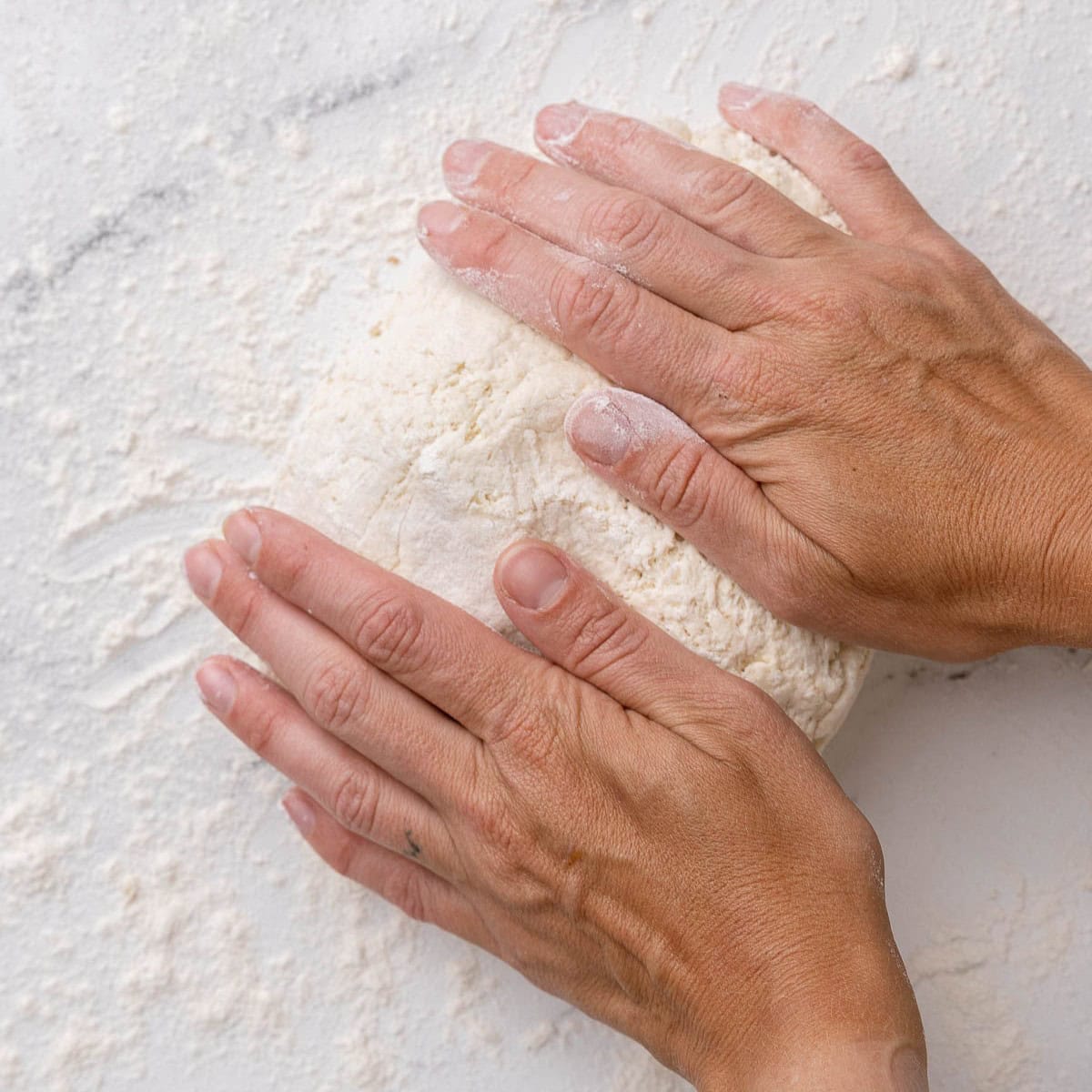 Hands kneading dough on a floured surface.