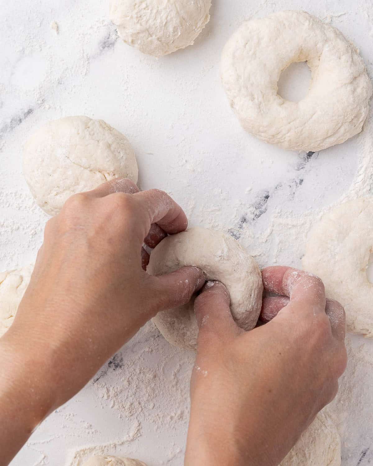 Dough balls after resting with hands shaping one on the surface.