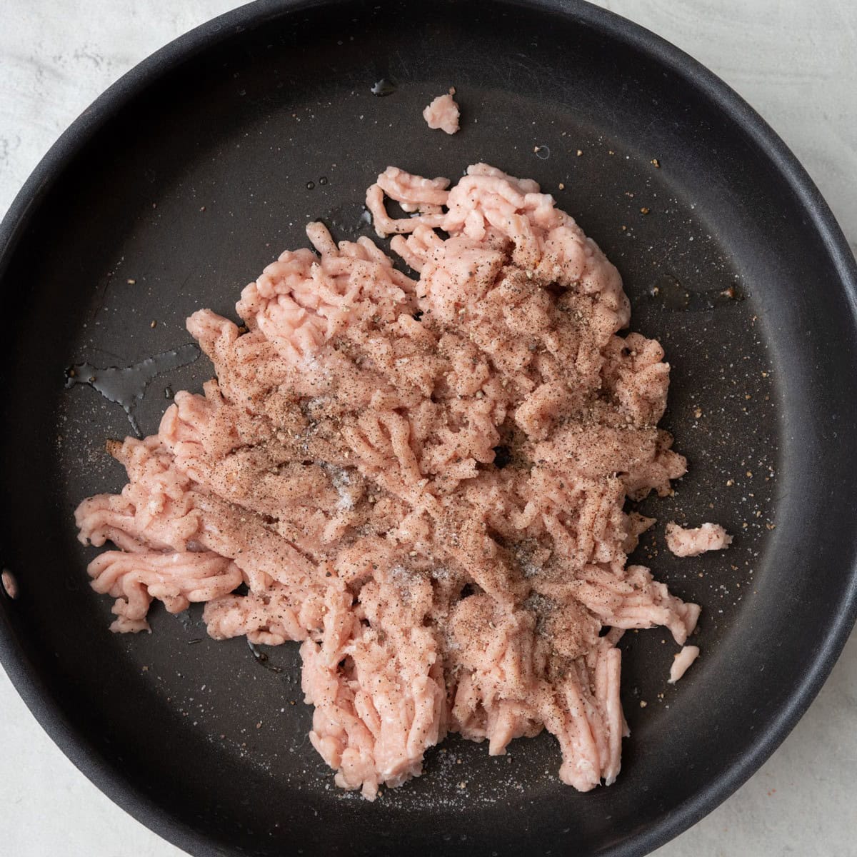 Ground chicken in a saucepan seasoned with salt and pepper before cooking.