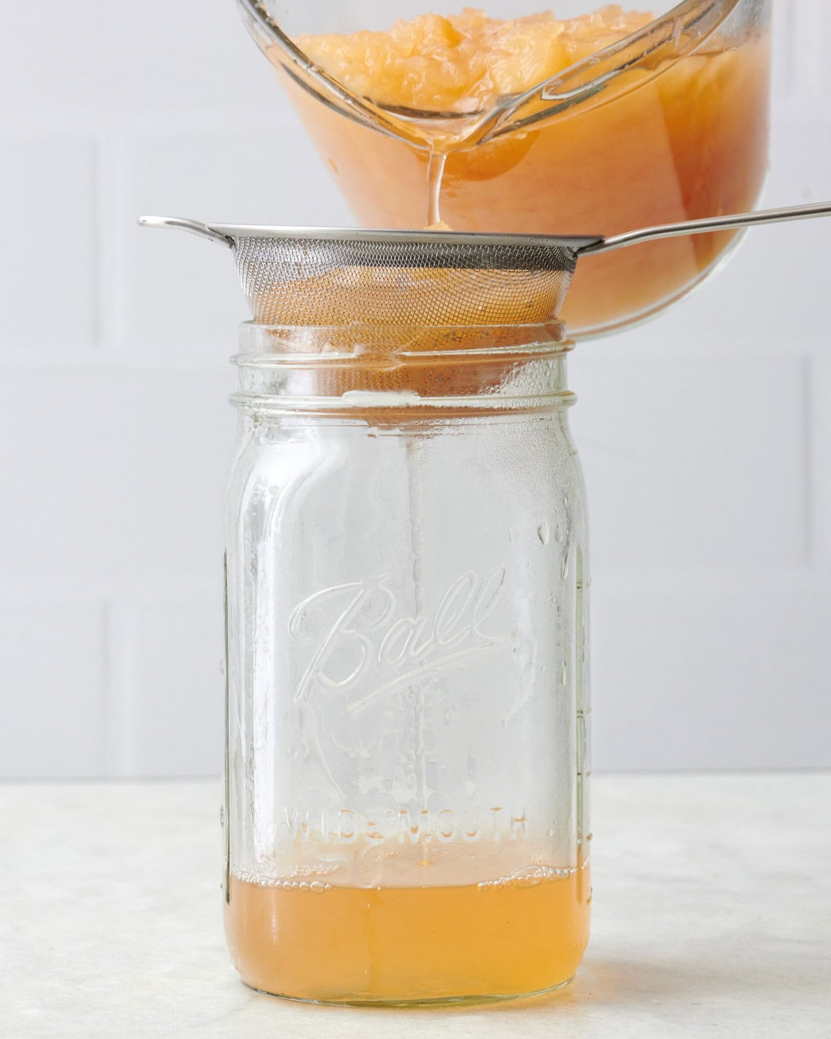 Pouring cider through a fine mesh sieve into 32-ounce clear mason jar.