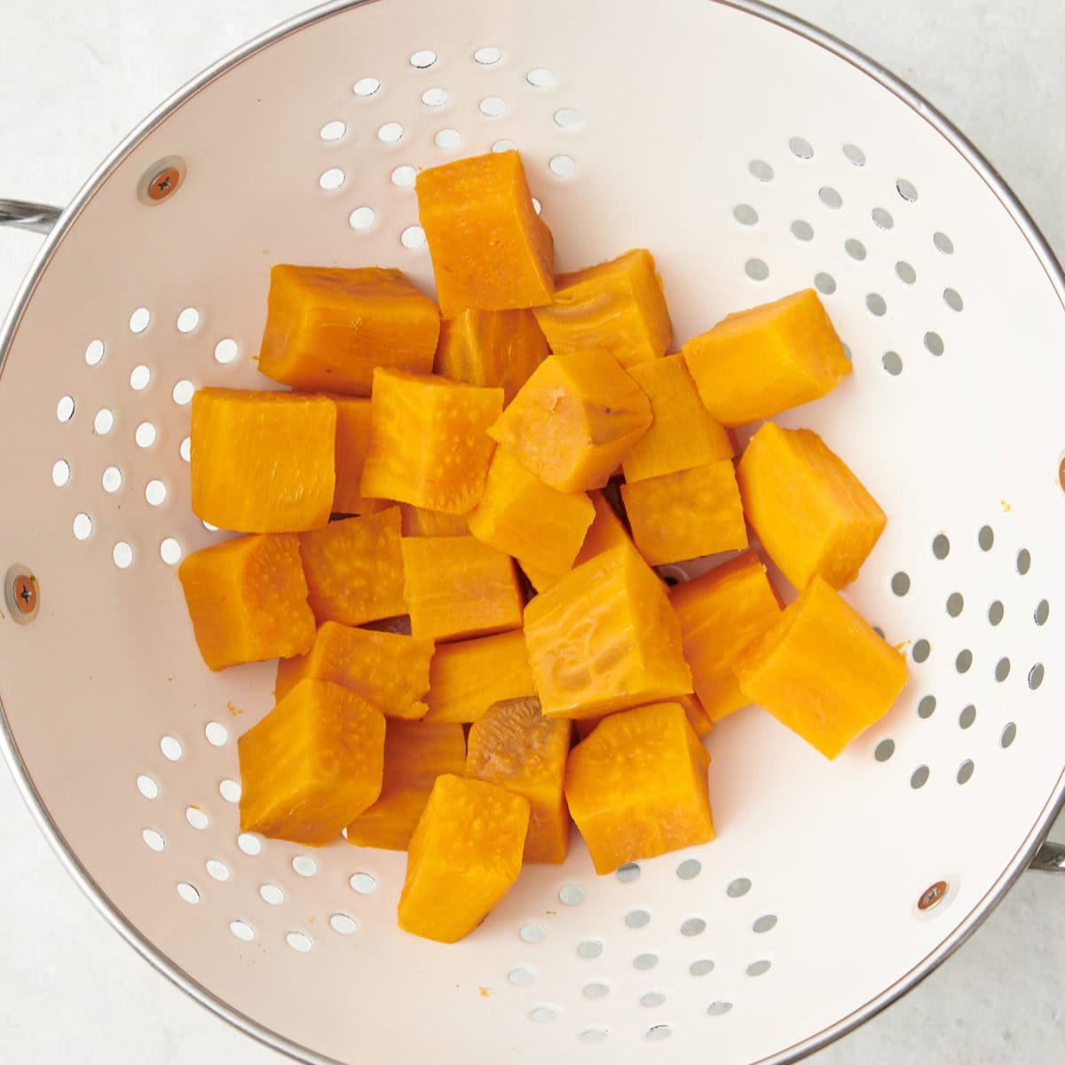 Sweet potato cubes in a colander after cooking with a fork piercing one to show doneness.
