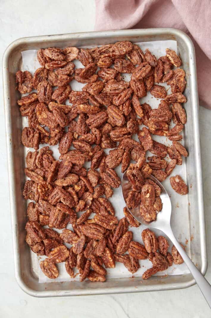 Toasted candied pecans on a baking sheet with a spoon scooping a few pieces.