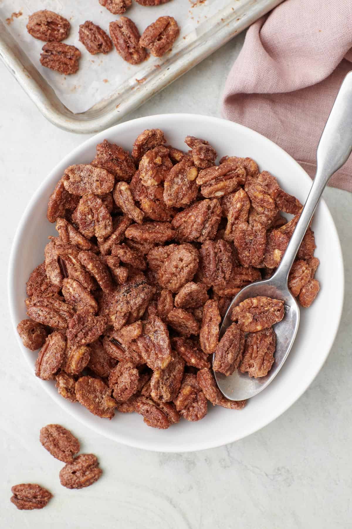 Candied pecans in a bowl with a spoon dipped in for serving.