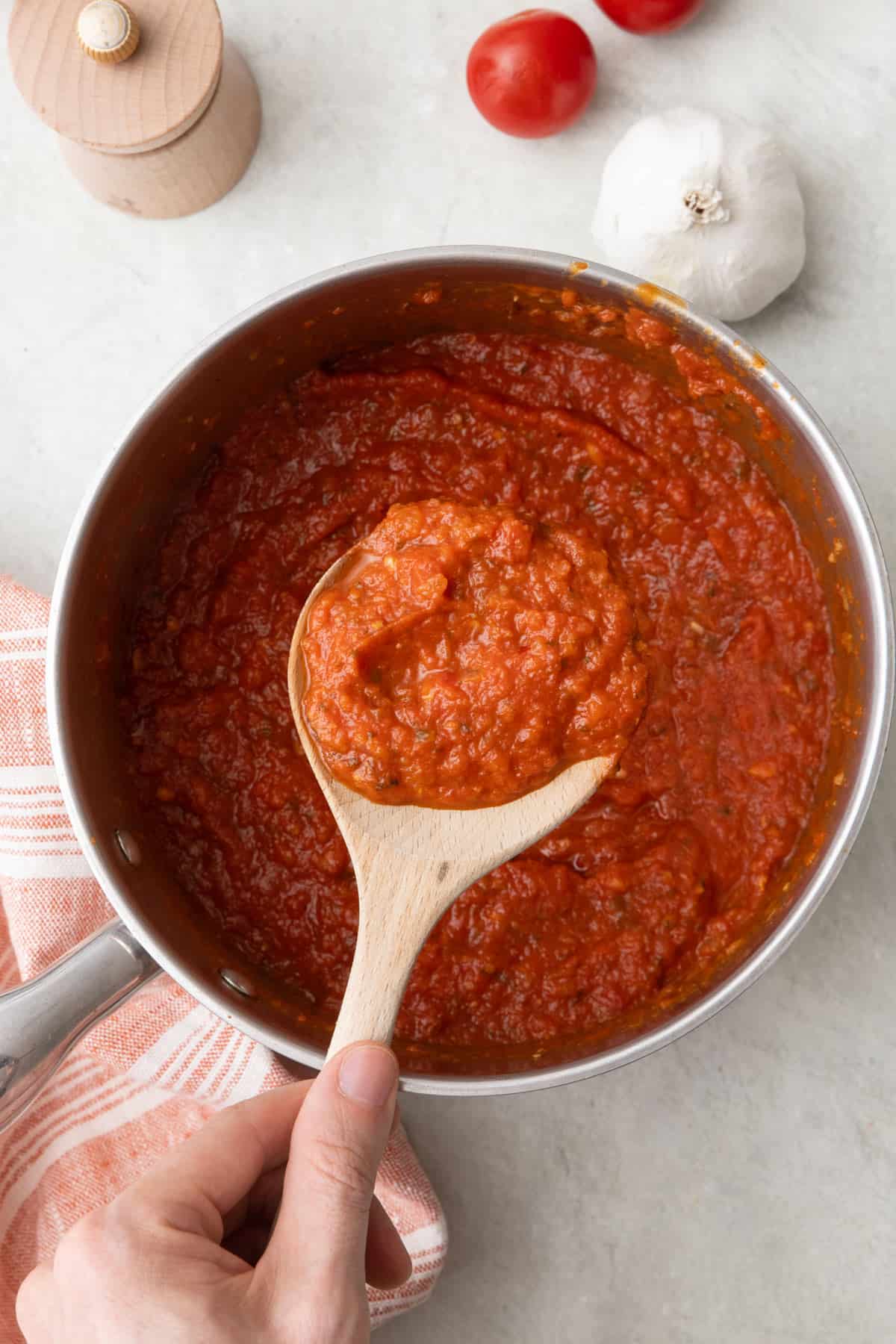 Spoon lifting up some pizza sauce from pot.