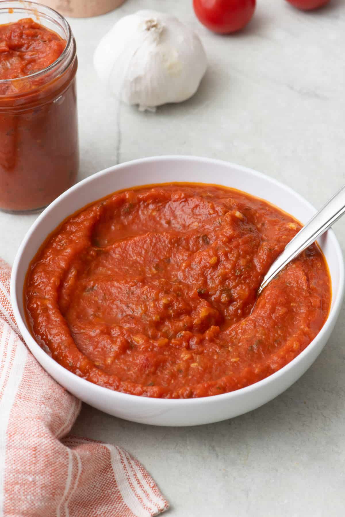Pizza sauce in a bowl with spoon dipped in and a small jar of sauce nearby.