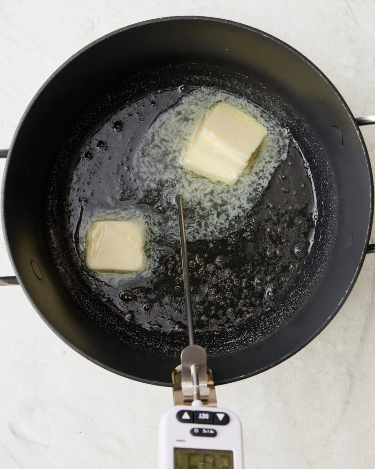 Butter added to boiling sugar with a candy thermometer now on the side of the pot.