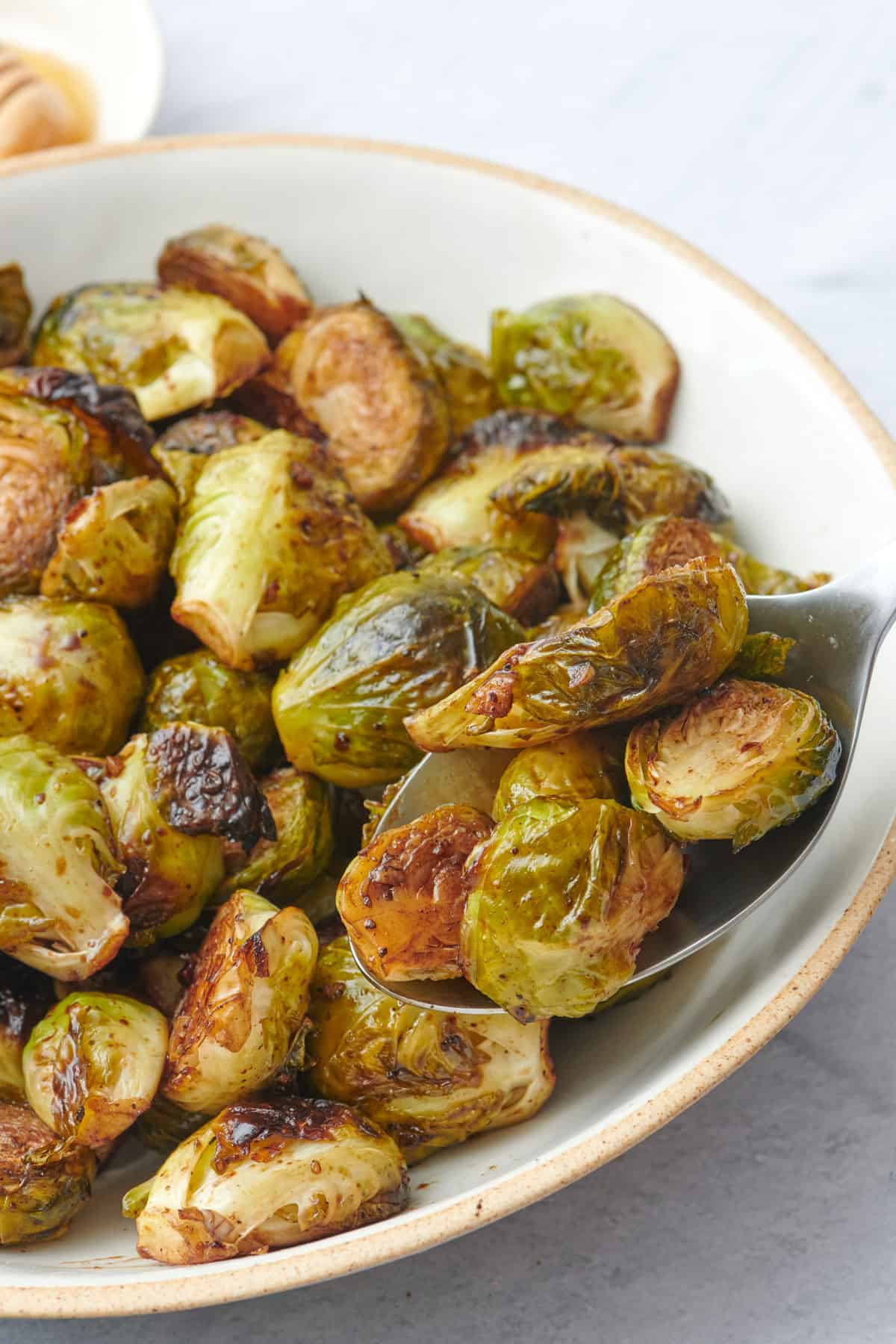 Spoon lifting up balsamic brussel sprouts from serving bowl.