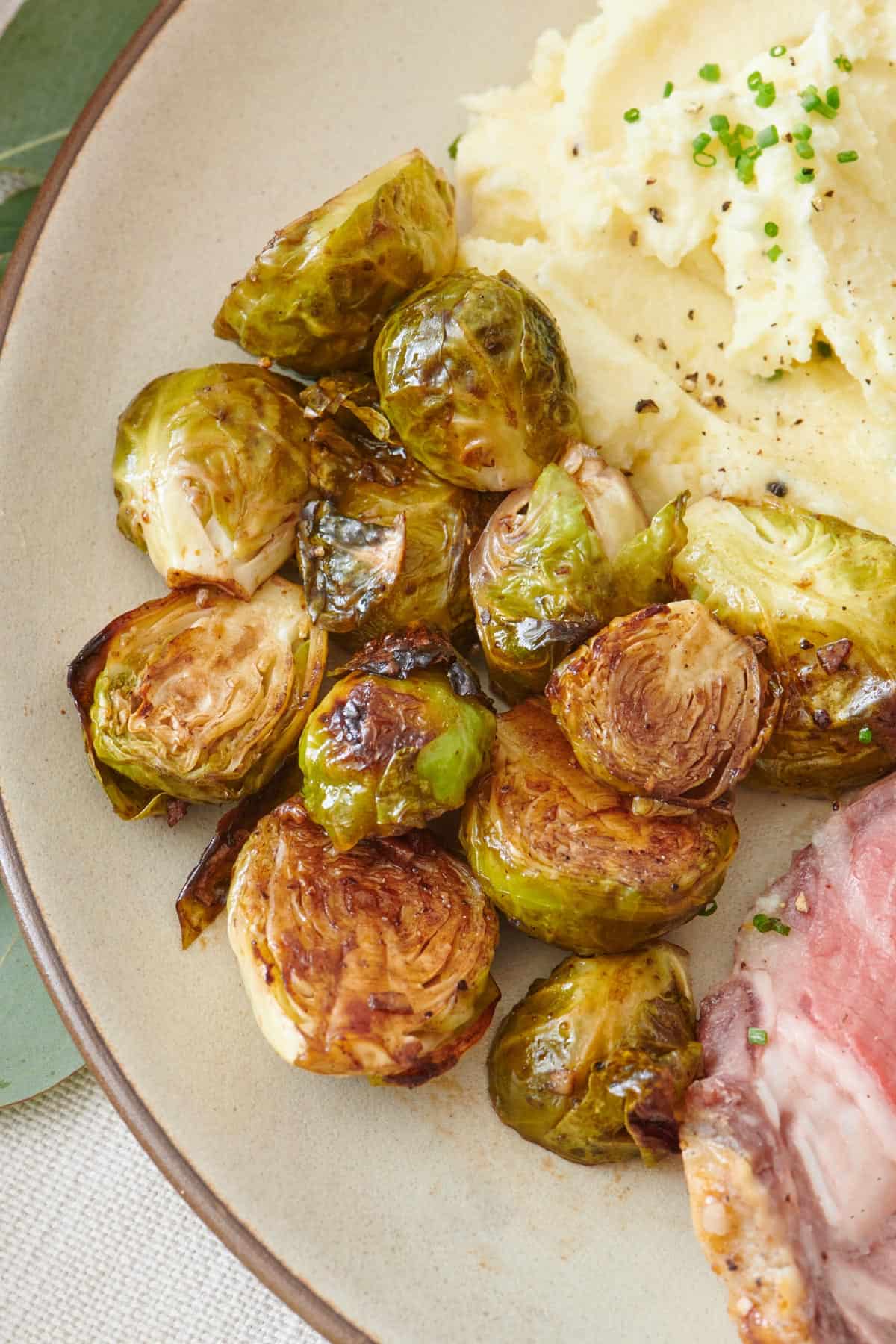 Roasted balsamic brussel sprouts on a plate with mashed potatoes and prime rib.