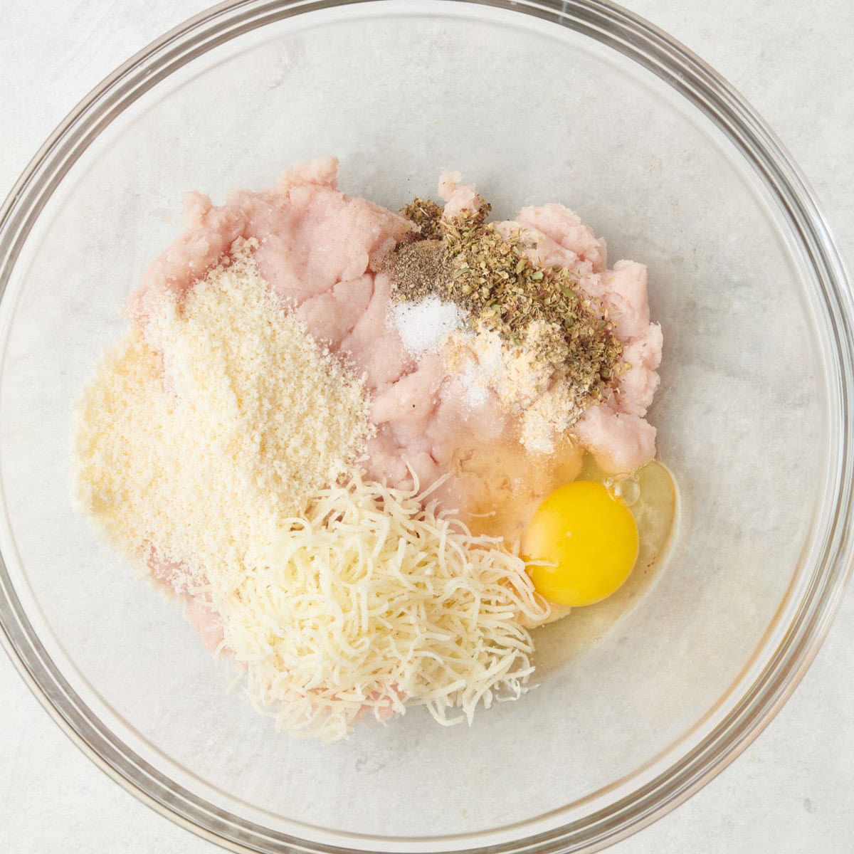 Parmesan, mozzarella, egg, and seasonings in a bowl on top of chicken before mixing.