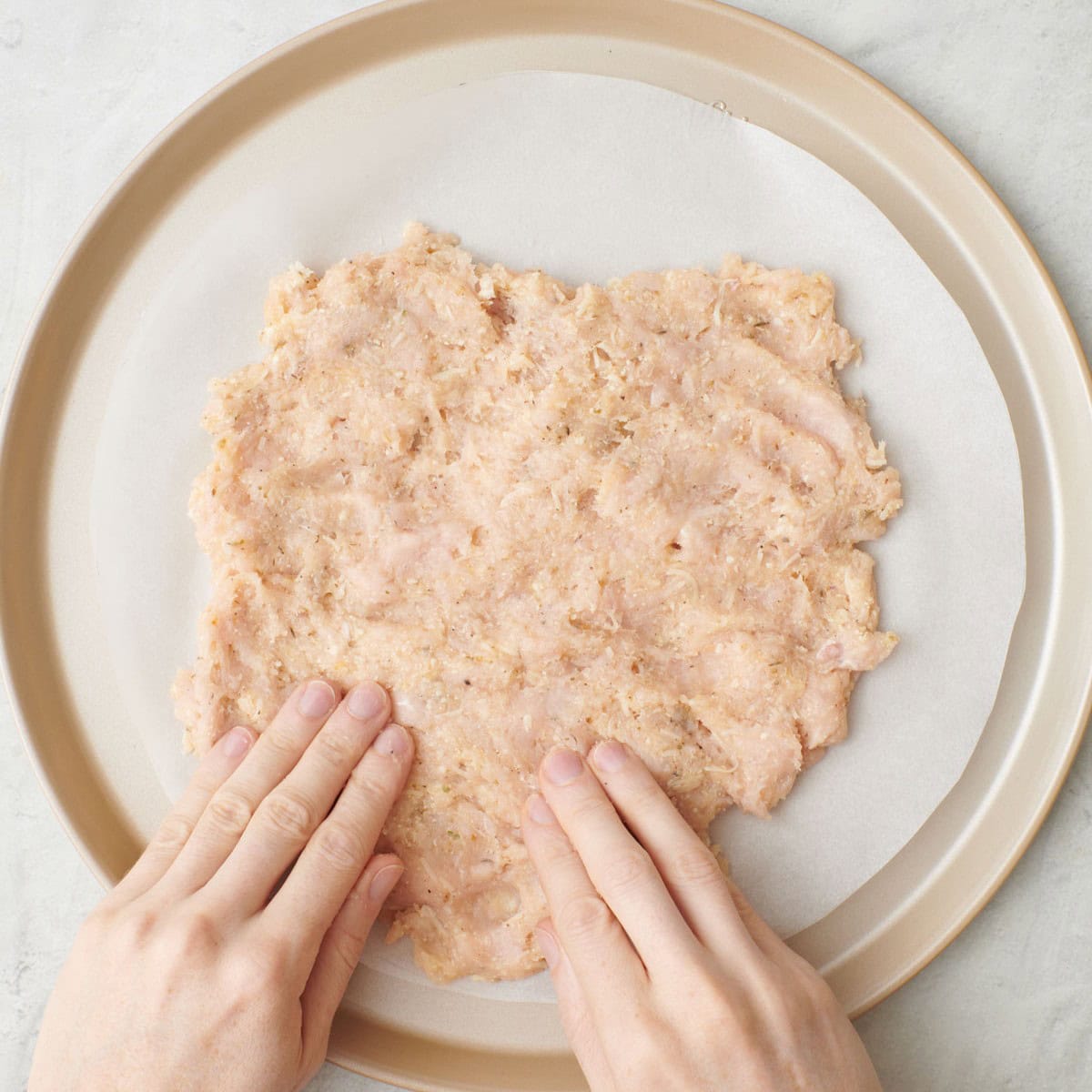Pressing chicken mixture on a prepared baking sheet.