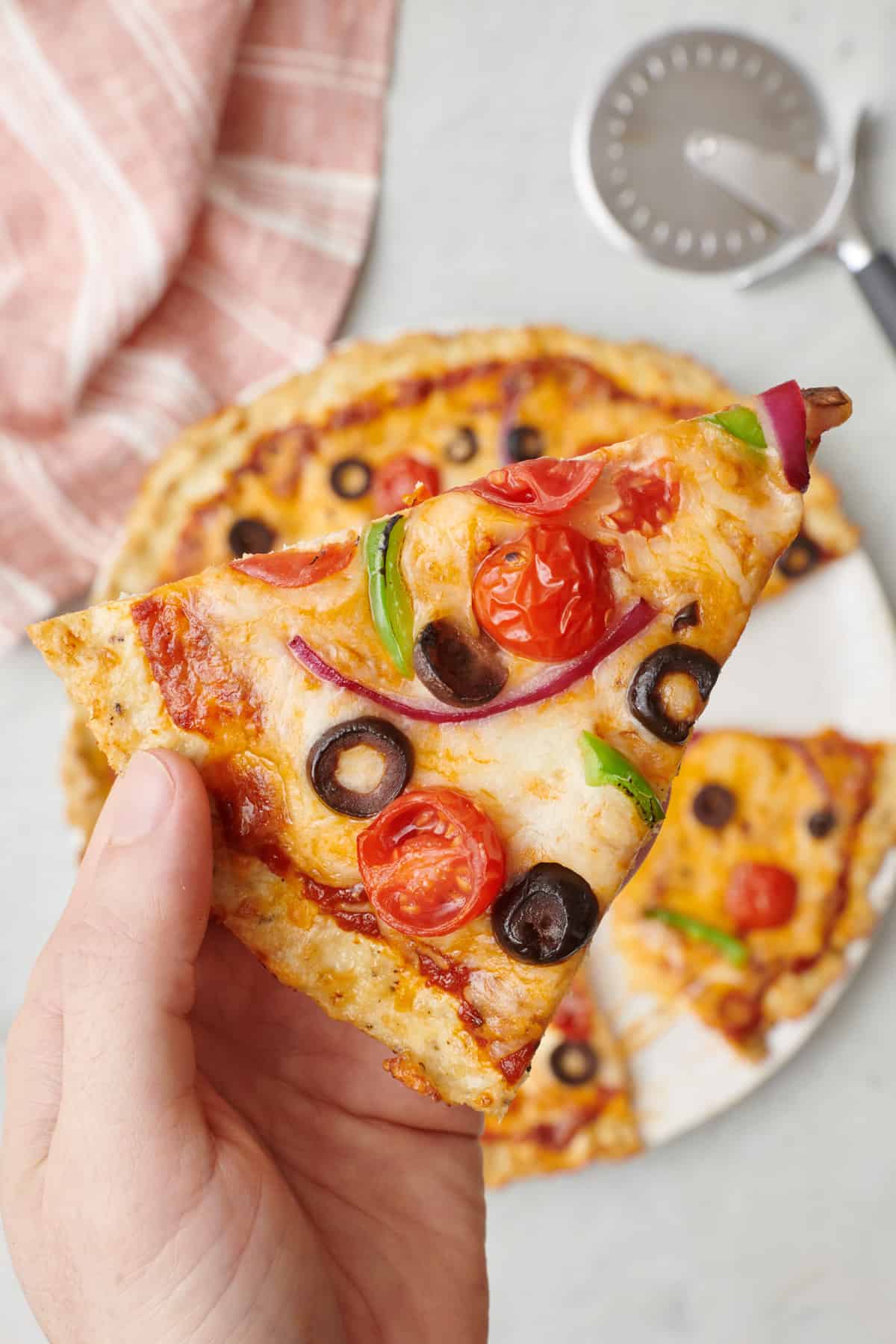 Hand holding a chicken crust pizza with toppings up close.