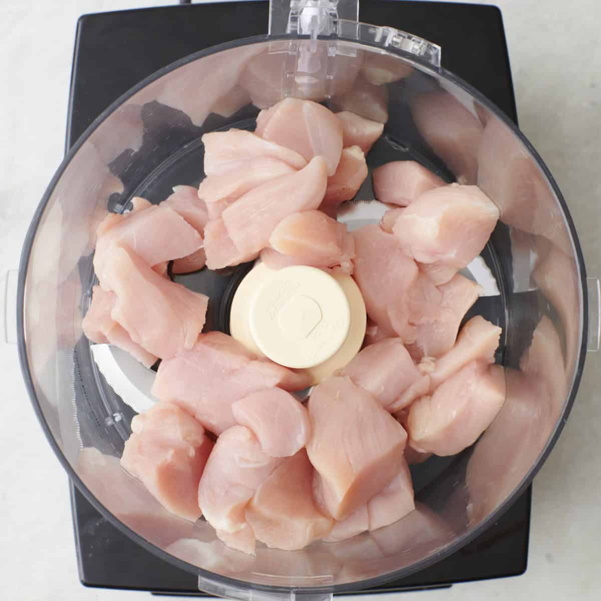 Chicken chunks in the bowl of a food processor before processing.