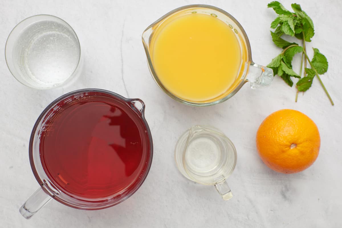 Ingredients for recipe in individual containers or whole: club soda, cranberry juice, orange juice, simple syrup, fresh orange, and fresh mint sprigs.