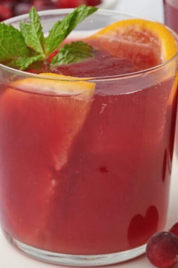 Cranberry orange mocktail in a glass with orange slices and fresh mint leaves.