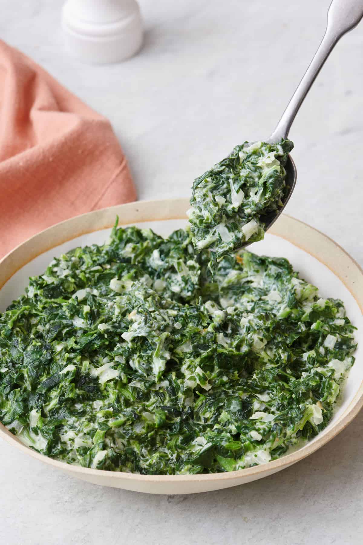 Spoon lifting up a serving of creamed spinach.