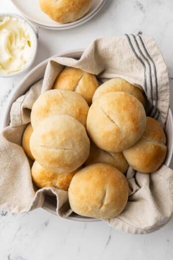 French bread rolls in a towel line bowl with a small dish of butter nearby.