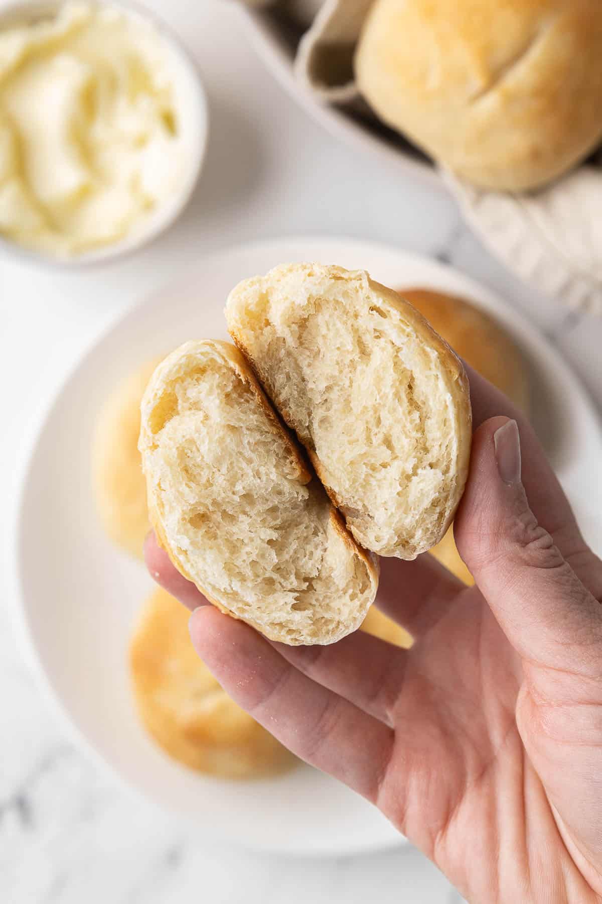 Hand holding a french bread roll that's cut in half to show the fluffy inside texture.