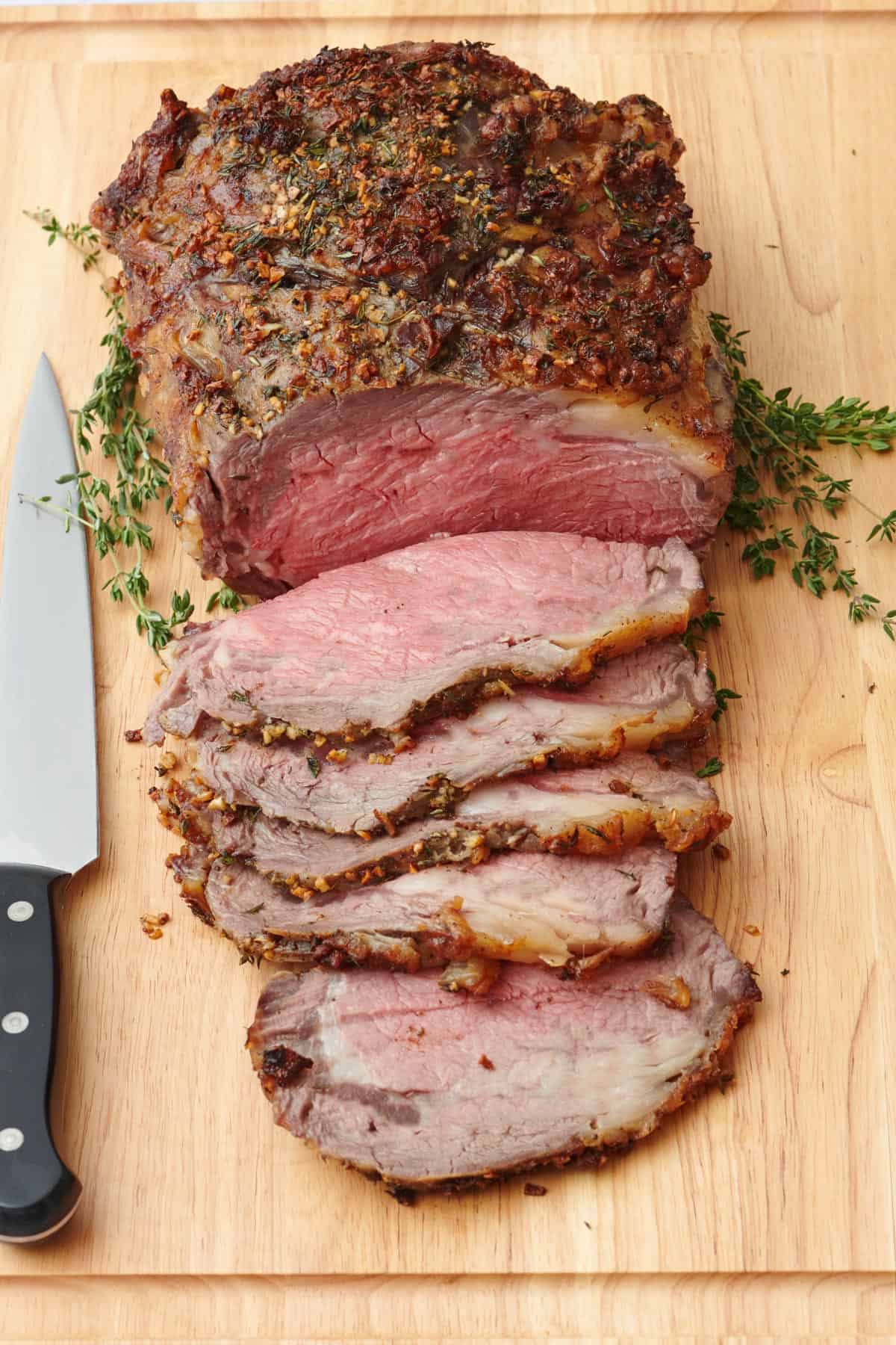 Garlic and herb crusted prime rib roast on a cutting board sliced halfway.