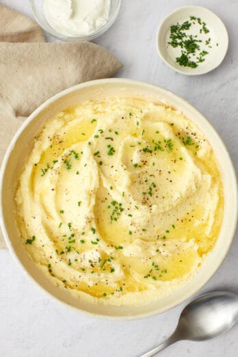 Greek yogurt mashed potatoes in a bowl, topped with melted butter and chopped herbs.