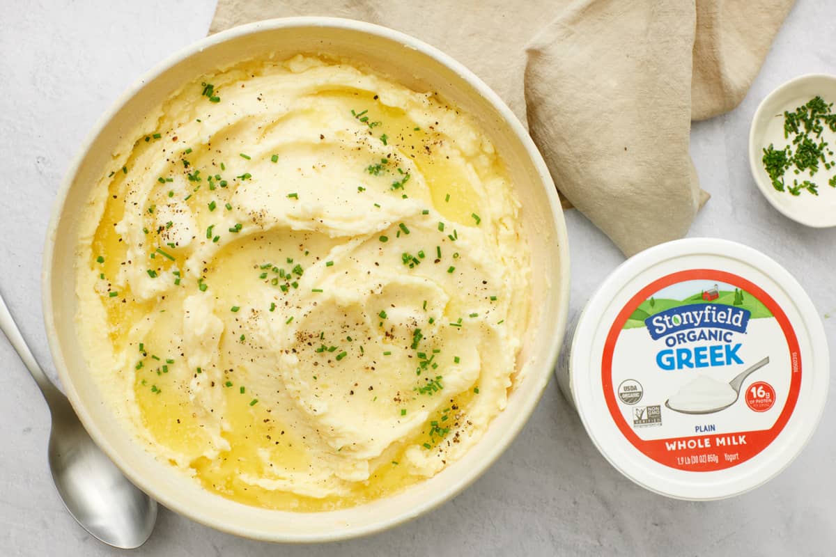 Stonyfield Whole Milk Organic Greek Yogurt mashed potatoes in a bowl with melted butter and the container of yogurt nearby.