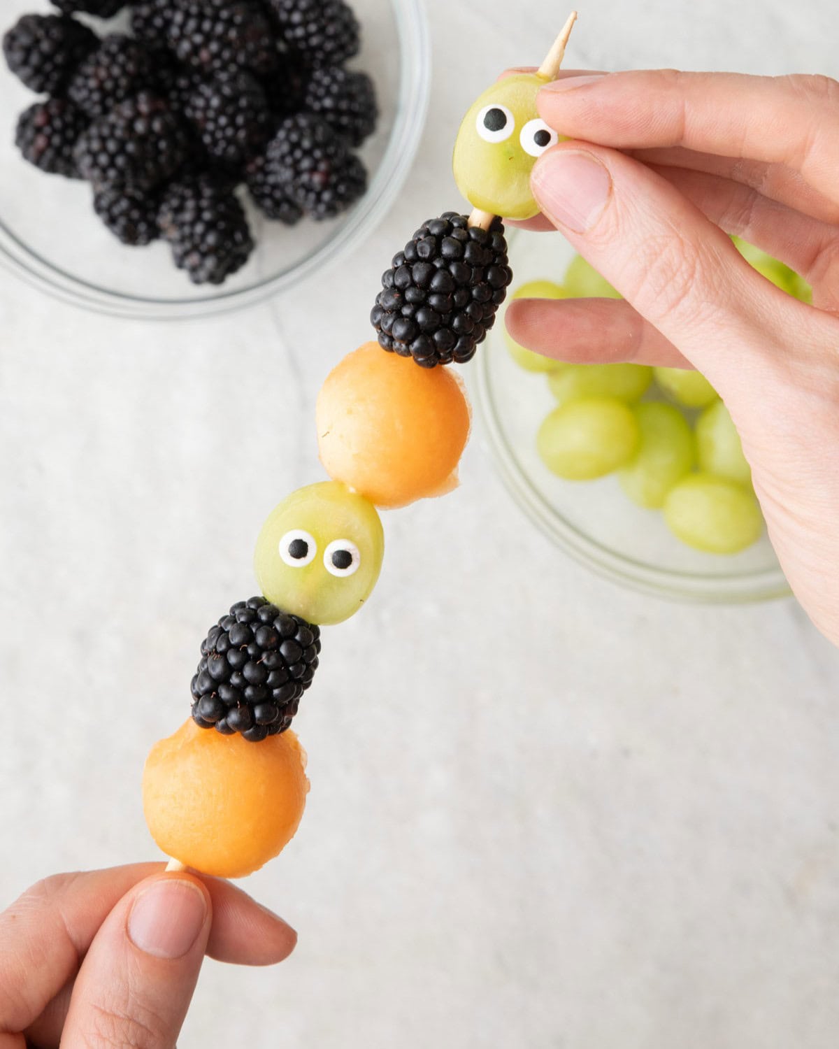 Adding candy eyeballs to grapes after skewered.