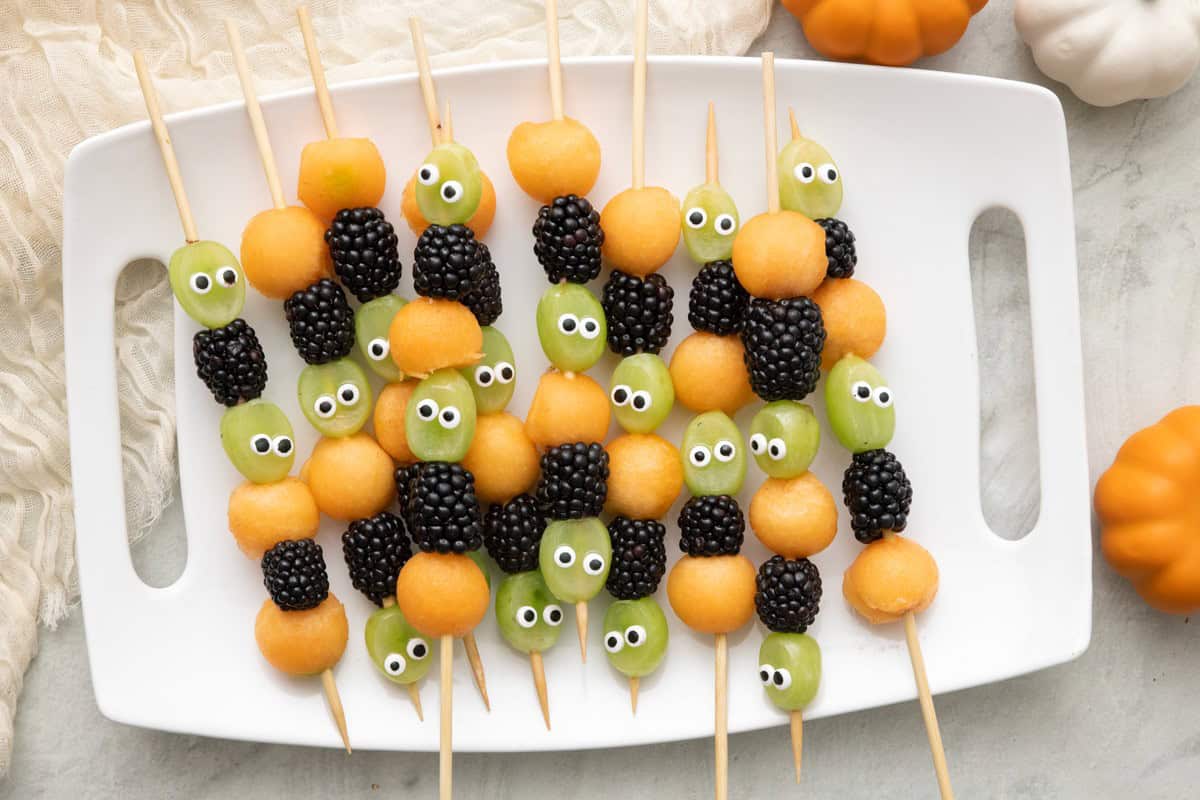 Halloween fruit kabobs on a tray with Halloween decor.