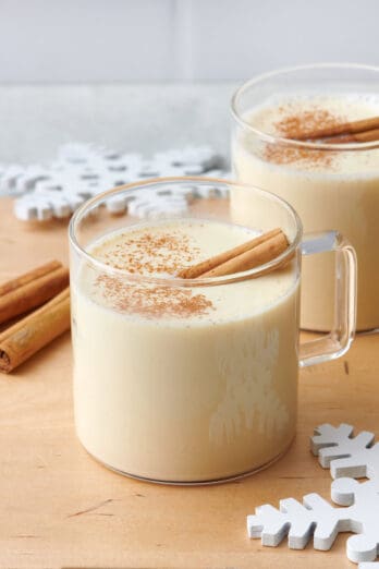 Two glasses of creamy eggnog with cinnamon stick inside.