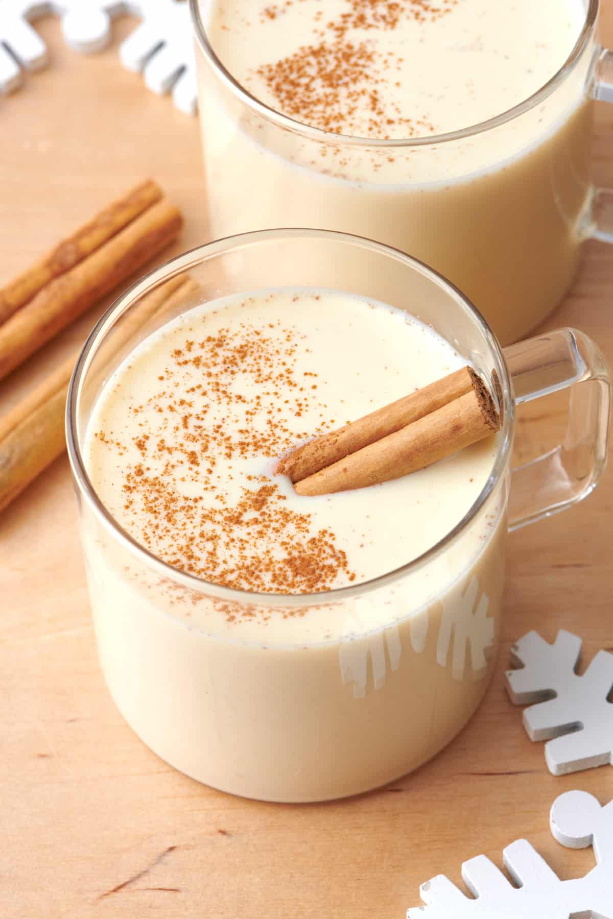 Homemade eggnog in a glass mug with a cinnamon stick inside and another glass nearby.
