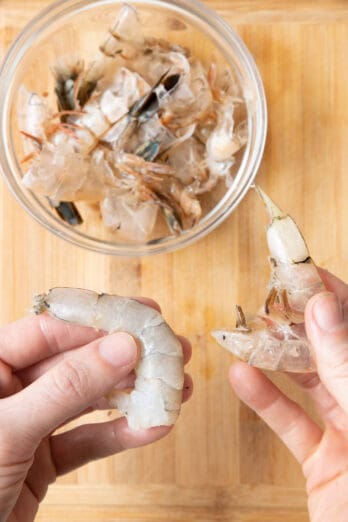 Hand peeling a jumbo shrimp with a small bowl of more shrimp shells.