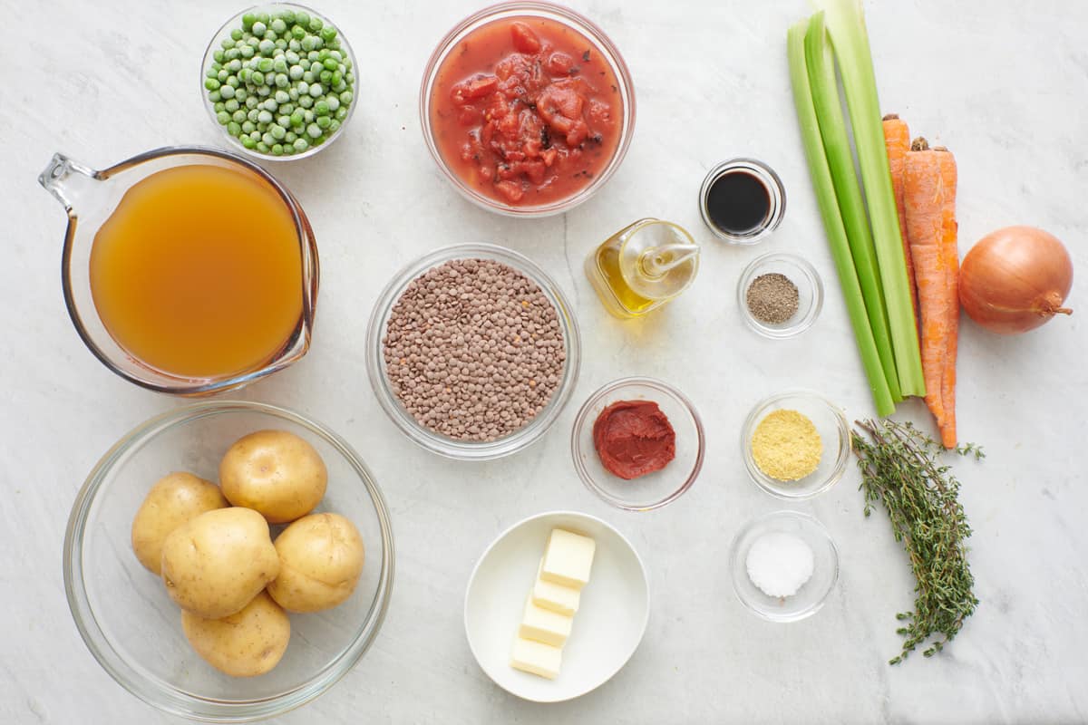 Ingredients for recipe before being prepped: frozen peas, vegetable stock, potatoes, fire roasted diced tomatoes, dry lentils, butter, tomato paste, oil, soy sauce, pepper, nutritional yeast, salt, fresh thyme, celery, carrots, and onion.